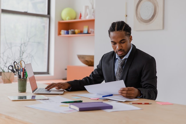 person reviewing document with their laptop open while sitting at their desk